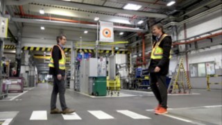 Two employees meet each other in the warehouse, wearing the Linde Secure Distance Vest and the Linde Distance Beeper. Two employees meet each other in the warehouse, wearing the Linde Secure Distance Vest and the Linde Distance Beeper.