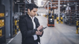 A Linde Material Handling employee stands in the warehouse and takes notes on his tablet.