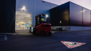 A Linde forklift truck equipped with the Linde TruckSpot reverses out of the hall at dusk.