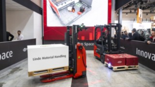 Two Linde MH trucks transporting goods. A digital representation of the trucks can be seen on a screen.