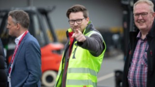 A man in a high-vis vest looks at and points his finger towards the camera 