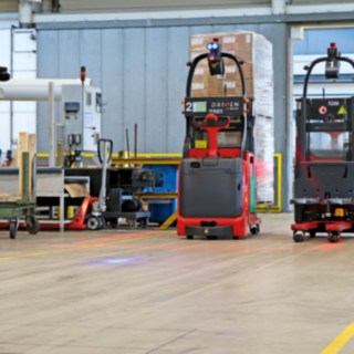 Two L-MATIC automatic high-lift trucks transport goods between the packaging line and the flow-through warehouse.