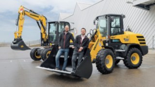 Dominik Haag and Markus Köhler from Yanmar Compact Equipment Europe standing in the bucket of an excavator.