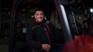 Employee of Linde Material Handling sits in a forklift truck and smiles at the camera.