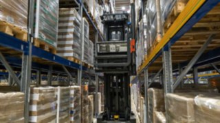 The Linde K-MATIC automated narrow-aisle forklift is driving through a rack aisle.